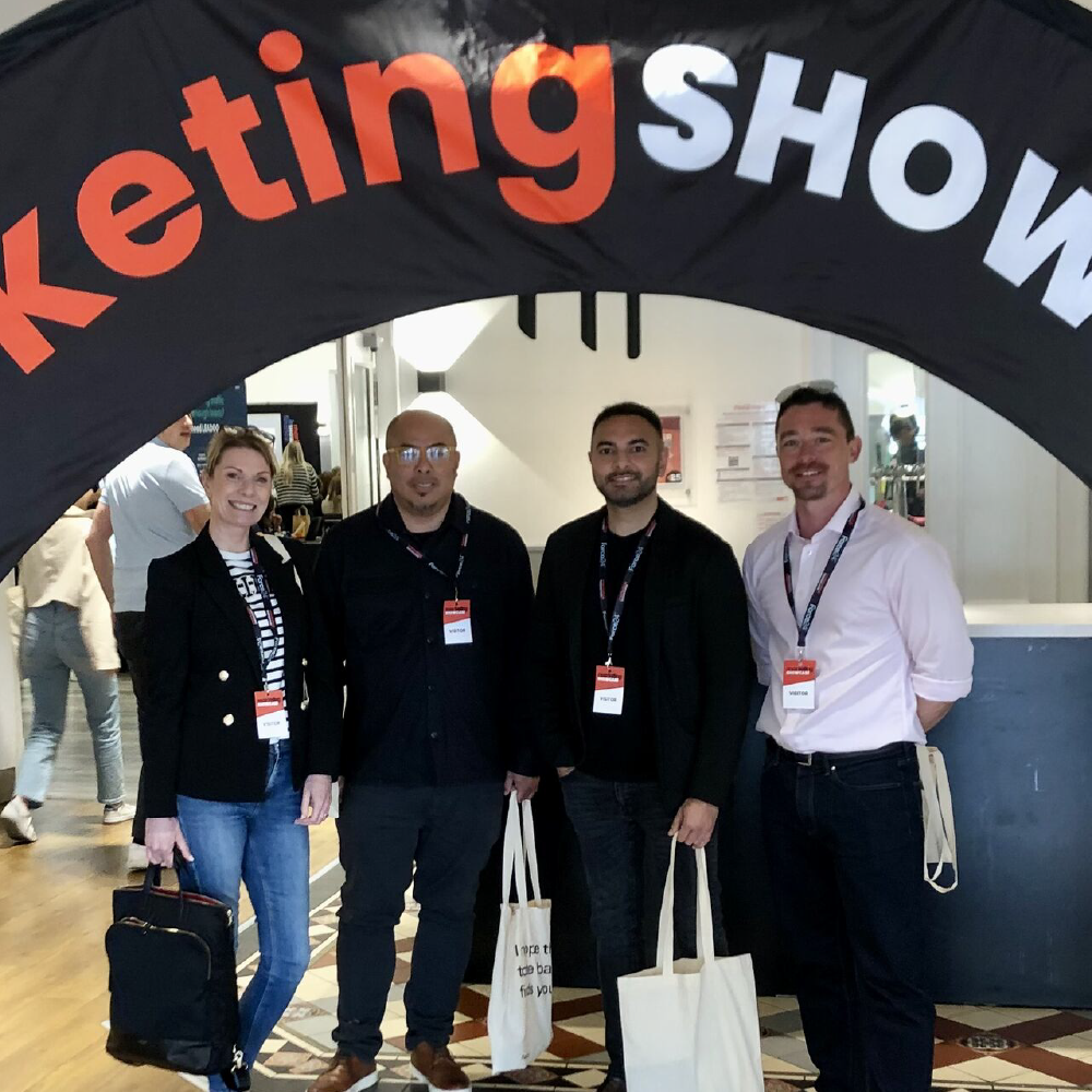 Zoe, Ian, Usmaan and Rich smiling at the camera under a marketing showcase banner