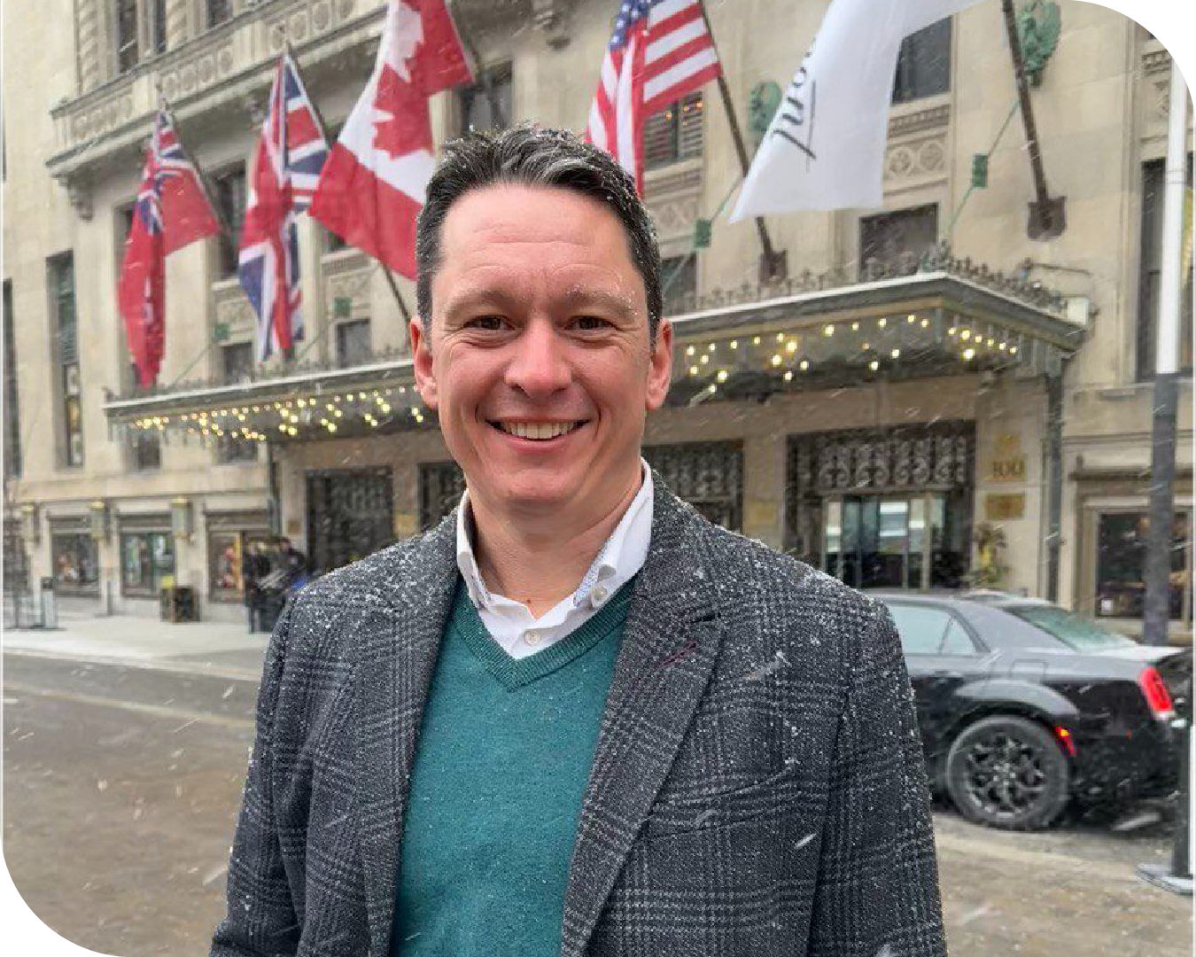 Mark Vernon, GV MD, standing on the street in the snow in front of a building with flags including the Canadian and British.