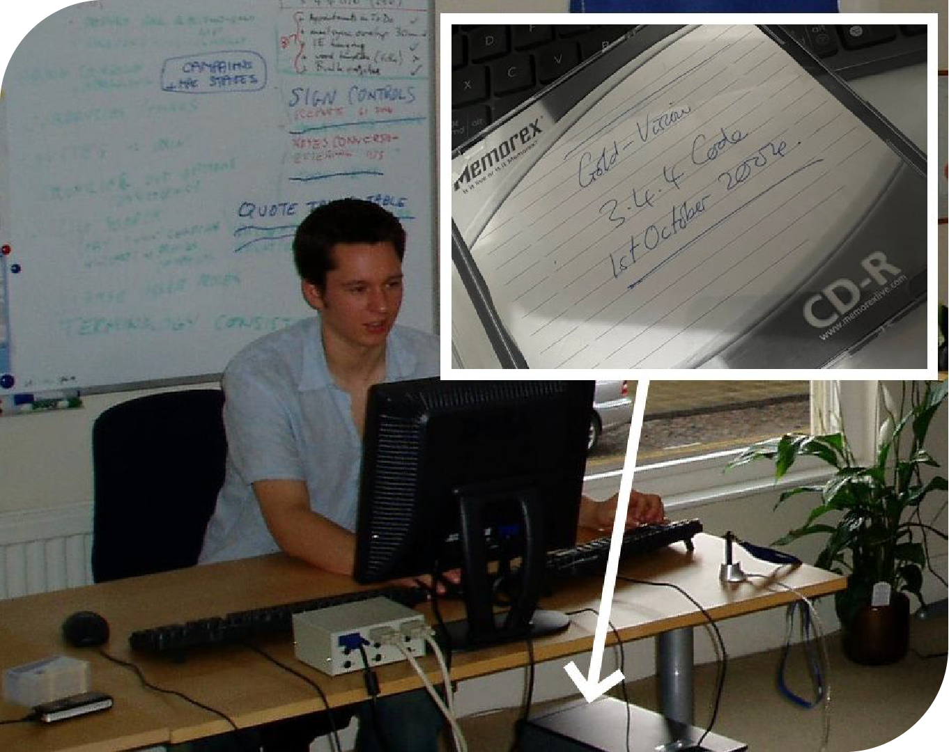 A picture of Mark from 20 years ago taken during the first release cut of Gold-Vision CRM that he was responsible for. Mark is sat at a desk with a desktop computer, with a whiteboard with processes written out behind him. 