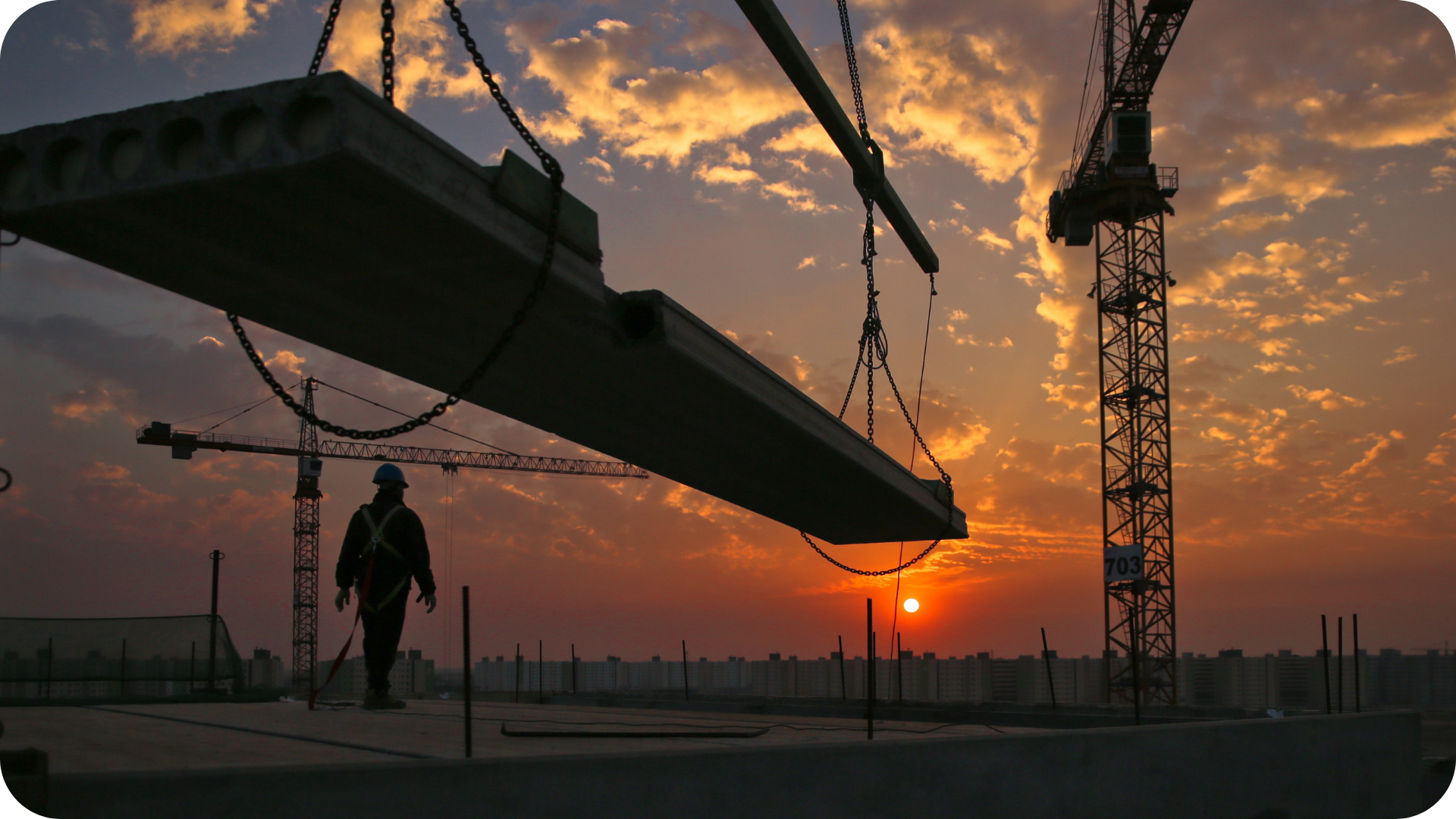 "Construction worker on-site at sunset with cranes lifting concrete beams, symbolising teamwork, coordination, and improved performance—aligned with boosting revenue through CRM in the construction industry.